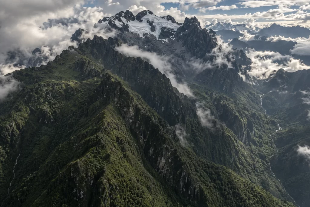 Fragmented white glacier ice clings to dark green Rwenzori mountain ridges beneath broken clouds.