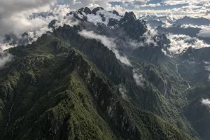 Fragmented white glacier ice clings to dark green Rwenzori mountain ridges beneath broken clouds.